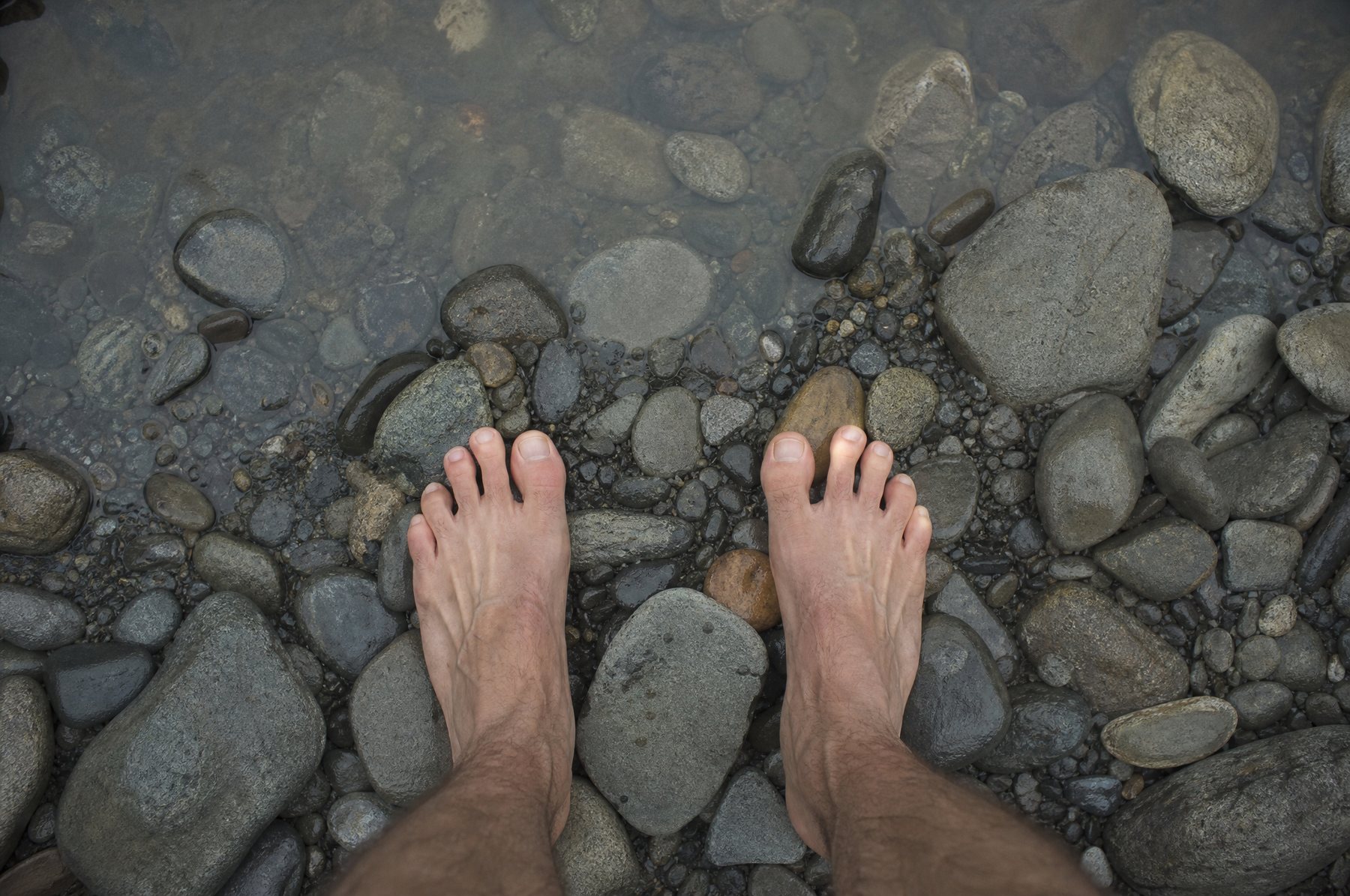 Bare feet standing on smooth river stones in clear shallow water
